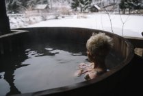 Vista lateral de mujer rubia con pelo corto nadando en la bañera de inmersión exterior en invierno . - foto de stock
