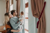 Felice famiglia che abbraccia con bambino alla finestra — Foto stock