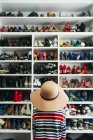 Visão traseira da mulher sentada na frente de prateleiras com sapatos diferentes — Fotografia de Stock