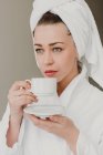 Задумчивая женщина пьет кофе после ванны и смотрит в сторону — стоковое фото