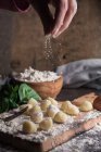 Crop female hand pouring flour on raw gnocchi at table — Stock Photo