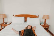 Junge Frau liegt und entspannt auf Bett im Hotelzimmer — Stockfoto