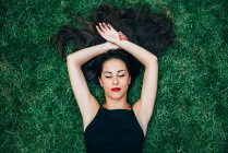Брюнетка жінка, що лежить в траві з закритими очима — стокове фото