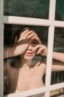 Donna in reggiseno in piedi alla finestra e toccare il viso nella giornata di sole . — Foto stock