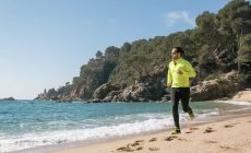 Uomo che fa jogging sulla spiaggia di sabbia e guarda il mare — Foto stock