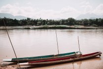 Barcos longos na costa com água suja em dia nublado . — Fotografia de Stock