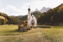 Piccola chiesa bianca sul prato verde in montagne coperte di foresta
. — Foto stock