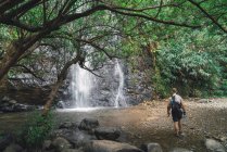 Rückansicht eines Touristen, der zum Wasserfall im Wald geht. — Stockfoto