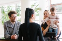 Happy family with child talking with woman working at reception in hotel — Stock Photo