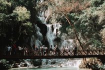 Laos, luang prabang: Touristengruppe steht auf Brücke und betrachtet Wasserfall im tropischen Wald. — Stockfoto
