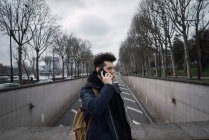 Jovem de pé e falando no smartphone na rua — Fotografia de Stock