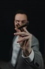 Close-up hand of handsome man in suit smoking cigar on dark background. — Stock Photo