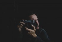 Photographer sitting over black and focusing with vintage camera — Stock Photo