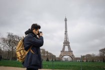 Vue latérale du jeune homme debout avec caméra et prise de vue de la tour Eiffel . — Photo de stock