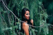 Pretty woman in fir branches flirting with camera — Stock Photo