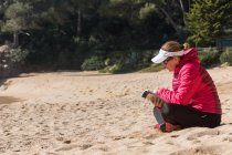 Вид сбоку зрелой женщины, читающей книгу на песчаном пляже — стоковое фото