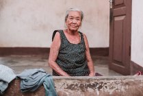 ЛАОС, ЛУАНГ ПБАНГ: Пожилая женщина сидит у дверей дома и смотрит в камеру . — стоковое фото