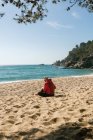 Задний вид зрелой женщины, читающей книгу на песчаном пляже — стоковое фото
