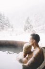 Embracing couple sitting in plunge tub in winter landscape — Stock Photo