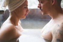 Side view of sensual tattooed couple sitting face to face in plunge tub in winter. — Stock Photo
