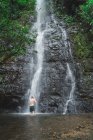 Rückansicht eines Mannes, der sich an einer Kaskade tropischer Wasserfälle wäscht — Stockfoto