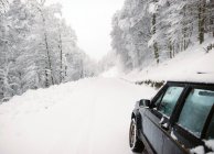 Image recadrée d'une voiture garée sur une route enneigée en hiver . — Photo de stock