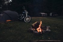 Ретро мотоцикл припаркован у костра на природе в вечернем сумерке — стоковое фото