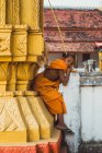 LAOS- 18 FÉVRIER 2018 : Jeune moine assis sur une clôture et regardant la caméra — Photo de stock