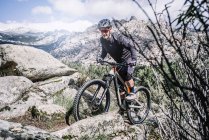 Biker maturo arrampicata collina rocciosa con mountain bike . — Foto stock
