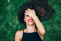 Fröhliche brünette Frau liegt im Gras und versteckt Gesicht — Stockfoto