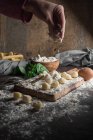 Erntehelfer gießen Mehl auf rohe Gnocchi am Tisch — Stockfoto