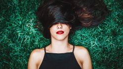 Allegro bruna donna sdraiata in erba con ciocca di capelli sopra gli occhi — Foto stock