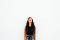 Young woman leaning on white wall and looking up — Stock Photo