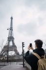 Vista traseira do jovem turista tomando fotos da torre Eiffel com telefone — Fotografia de Stock