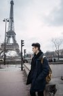 Young man standing on background of Eiffel tower on cloudy day — Stock Photo