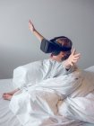 Симпатичный мальчик играет в виртуальные очки на кровати — стоковое фото
