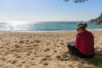 Mulher madura lendo livro na praia iluminada pelo sol — Fotografia de Stock