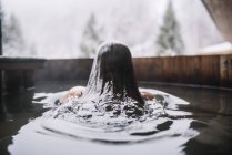 Back view of woman swimming out of outside plunge tub in winter nature. — Stock Photo