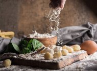 Crop hand pouring flour on raw gnocchi at wooden board — Stock Photo