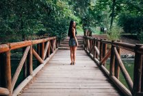 Hübsche junge brünette Frau steht auf Holzbrücke und blickt über die Schulter in die Kamera. — Stockfoto