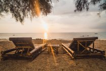 Two empty loungers on sand beach at sunset — Stock Photo