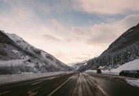 Perspective view to asphalt road in snowy hills in winter day. — Stock Photo