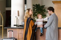 Молода сім'я з дитиною, що стоїть на рецепції готелю — стокове фото