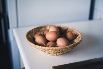 Straw-made bowl with brown chicken eggs on white table. — Stock Photo