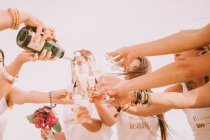 Group of pretty women friends standing together and pouring champagne in cloudy day. — Stock Photo