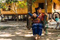 CHIANG RAI, TAILANDIA - 12 DE FEBRERO DE 2018: Mujer étnica sentada en columpios con niño - foto de stock