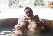Sensual pareja tatuada sentada en una bañera profunda y tomando selfie - foto de stock