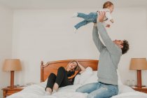 Father playing with child while mother lying and resting on bed in hotel. — Stock Photo