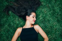 Fröhliche brünette Frau, die im Gras liegt und zur Seite schaut — Stockfoto