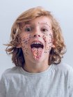 Cheerful boy with confetti on face showing tongue — Stock Photo